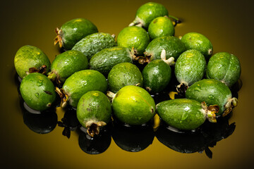 several feijoa fruits scattered on dark glass with gradient background