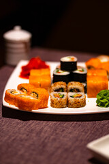 Serving of appetizing sushi on white plate in cafe. Close up of set of tasty sushi rolls with wasabi and ginger in traditional Japanese restaurant.