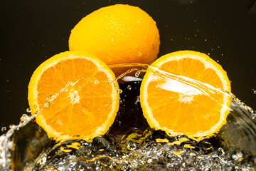 Fototapeta na wymiar two oranges, whole and cut in half with drops and splashes of water on dark glass with gradient background and reflection