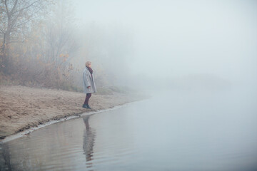 A girl runs along the shore of the lake in a foggy morning. She is having fun and has a good mood
