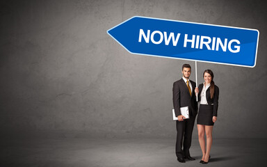 Obraz premium Young business person in casual holding road sign with NOW HIRING inscription, new business direction concept