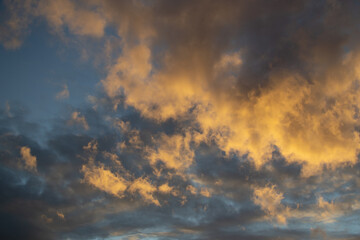 Sunset evening blue sky with fluffy light orange yellow clouds against a background of dark clouds. Different shapes