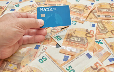 Bank card held by the hand of a white or Caucasian man on a bed of fifty euro bills