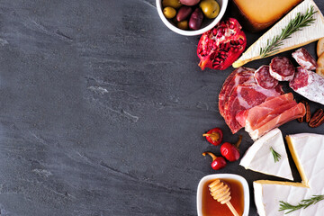 Assorted cheese and meat appetizers. Above view side border on a dark slate background with copy space.