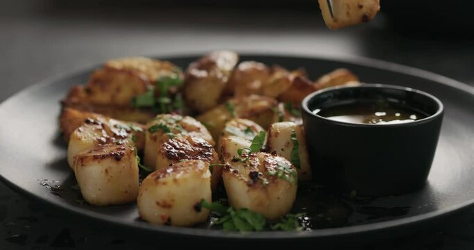 Slow motion eat roasted scallops with baked potatoes on black plate