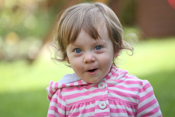 Close Up Portrait of a little 18 Month Old Girl with  Big Blue Eyes and Curly Hair, a girl Playing Outside, Funny Face Expression, Happy baby