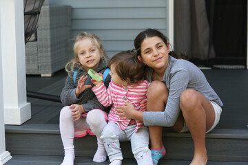 Three sister, girls sitting on the Porch. 3 girls, sisters, girlfriends. Happy Family Portrait, 18 month Old Toddler girl, 4 years Old blonde Girl and 9 years Old girl with brown hair