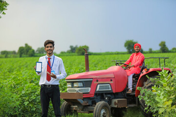 young Indian agronomist showing smartphone or tablet at field