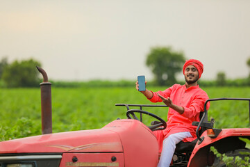 young Indian farmer showing smartphone or tablet on tractor