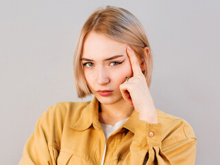 Displeased woman with blond hair thinking,face leaning on finger,looking straight,angry and stressed out