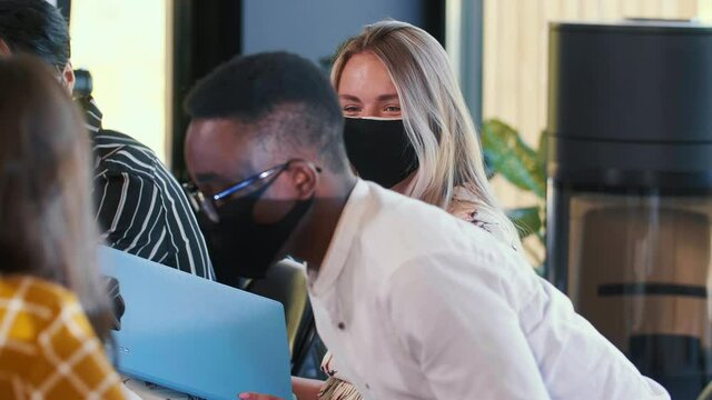 Business after coronavirus crisis. Close-up happy smiling multiethnic young managers work at office table in face masks.