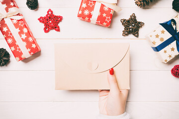 Top view of female hand holding an envelope on wooden background. New Year decorations. Christmas time concept
