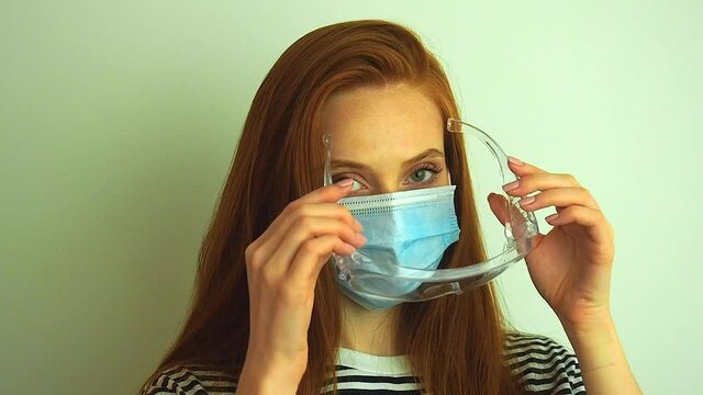 young woman wears protective white medical mask ,puts on medical gloves and glasses preparing for coronavirus epidemic