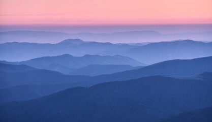 Mountain ridges in fog at sunset in autumn. Beautiful landscape with foggy mountain valley, rocks,...