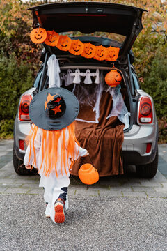Trick or trunk. Trunk or treat. Little child in Halloween witch hat walk to decorated trunk of car for candies. New trend and alternative safe outdoor celebration of traditional holiday.