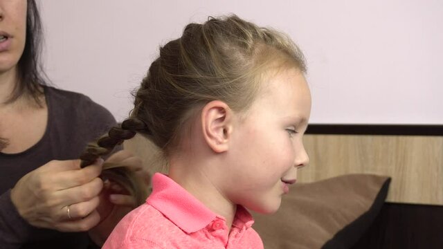 Young mother braids her beautiful little daughter's braid. A girl of about five years old sings songs in close-up. 4K