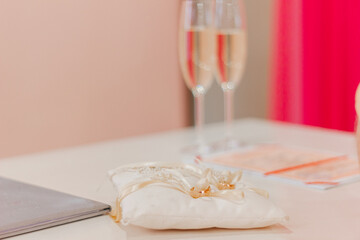 Wedding photography. Wedding rings on a white pillow close-up. Two glasses of champagne against the background of wedding rings.