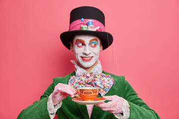 Horizontal shot of smiling cheerful mysterious hatter spends free time on tea party wears hat and...