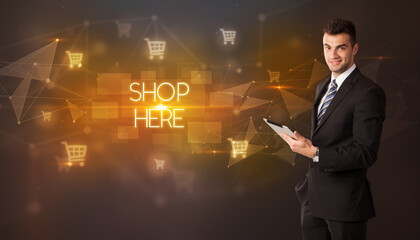 Businessman with shopping cart icons and SHOP HERE inscription, online shopping concept