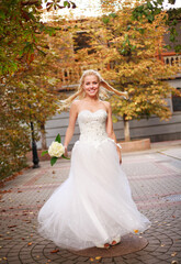 Fototapeta na wymiar Young happy bride in wedding white dress in autumn yard whirl emotionally