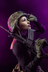 Fototapeta premium a woman in a military airsoft uniform with an American automatic rifle and a helmet on a dark background