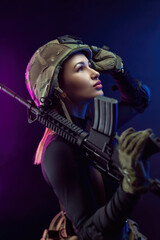 Obraz na płótnie Canvas a woman in a military airsoft uniform with an American automatic rifle and a helmet on a dark background