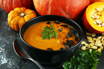 Roasted pumpkin and carrot soup with cream and pumpkin seeds on wooden background.