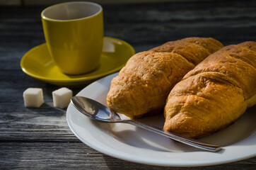 Still life with cup of coffee and croissant on the wooden background. Old retro camera and postcard are near the cup.