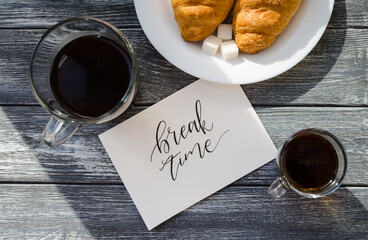 Still life with cup of coffee and croissant on the wooden background. Old retro camera and postcard are near the cup.
