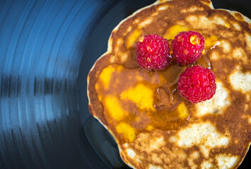 Pancake with fresh raspberries and honey on a dark background. Gramophone record. View from above. Closeup. Food, breakfast