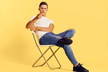 Cute man sitting on a chair white t-shirt jeans lifestyle modern style yellow background