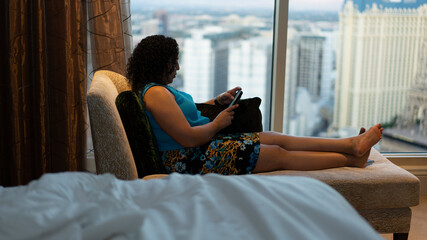 Beautiful Biracial, multiracial woman sits on chase in hotel room in business suit