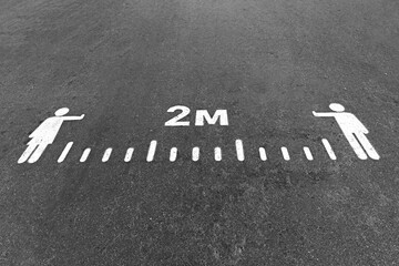 Fototapeta premium White painted 2 meters social distance sign on an asphalt road, pavement