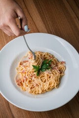 Spaghetti bolognese on a white plate with ground beef and tomato sauce. Pasta with bolognese sauce on a wooden background. Female hand holding pasta wrapped in a fork.