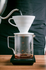 Dripping coffee with his hand, Barista pours water on ground coffee with a filter. Coffee shop worker standing at the counter with hand drip coffee set.