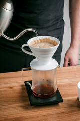 Dripping coffee with his hand, Barista pours water on ground coffee with a filter. Coffee shop worker standing at the counter with hand drip coffee set.