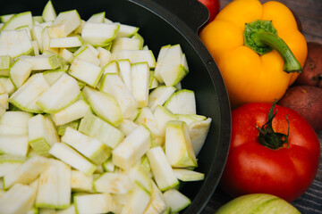 Sliced green zucchini. Red tomatoes and colored bell peppers on a dark wooden background. Raw vegetables. Young potatoes and radishes.