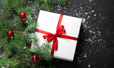 Christmas, New Year black stylish background with a branch of fir tree snow and snowflakes and a white gift box red bow and balls. Flat lay Nobody. Copy space