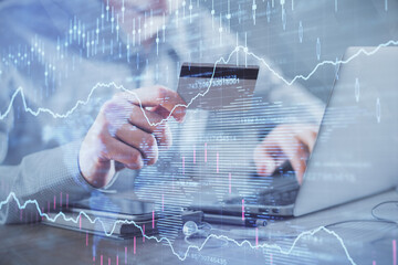 Double exposure of man hands holding a credit card and Forex graph drawing. Stock trading and digital fintech in Internet E-commerce concept.