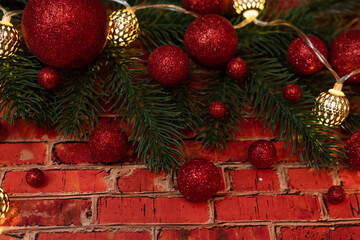Red brick background decorated with red Christmas balls. Christmas tree branches decorated with a garland. Christmas lights on red brick background
