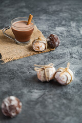 Hot chocolate with cinnamon on sackcloth. Mini doughnuts in the shape of a ball, filled and wrapped in recycled paper. Dark grey marble background. Christmas background. Breakfast.