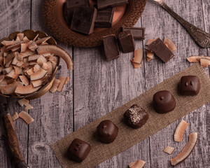 Assorted chocolate handmade praline on dark moody rustic background with dark chocolate chunks and coconut in a shallow background