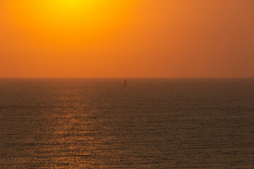 Velero en el horizonte en un atardecer brumoso.