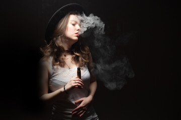 Young beautiful brunette Smoking an electronic cigarette with smoke on a dark background. The girl smokes VAPE. A woman lets out smoke from an electronic cigarette.