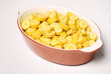 Raw cut yellow carrot in baking dish on white wooden table, closeup