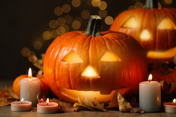 Pumpkin jack o'lanterns, autumn leaves and candles on table against blurred background. Halloween decor