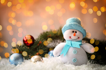 Cute snowman and fir tree branches with Christmas balls on snow, bokeh effect. Space for text