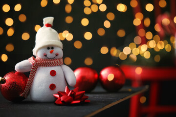 Cute snowman, bow and Christmas balls on table, bokeh effect. Space for text