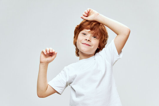 Cheerful red-haired boy holding hands on his head white t-shirt kfk gray background 