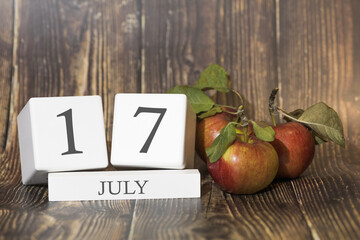 July 17. Day 17 of month. Calendar cube on wooden background with red apples, concept of business and an important event. Summer season.